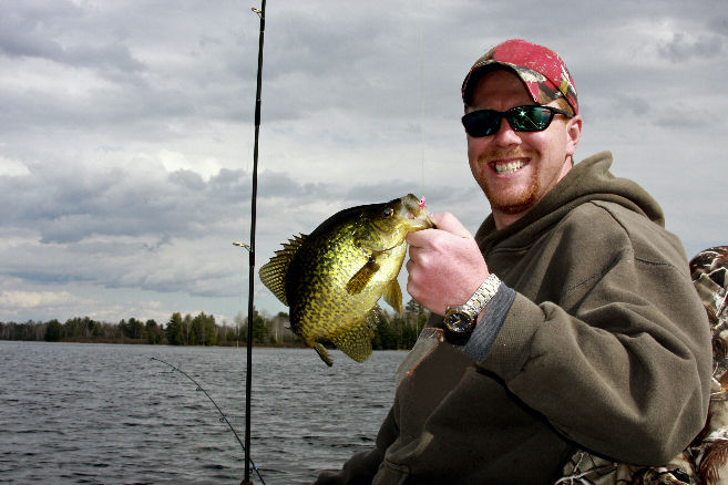 a man holding a crappie while sitting on a boat
