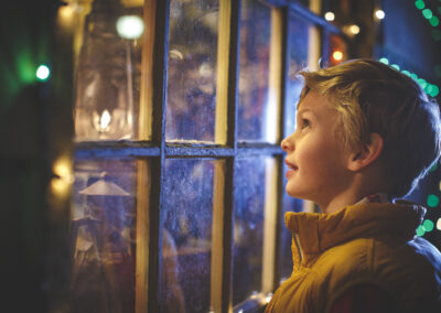 a young boy looking out the window at christmas lights